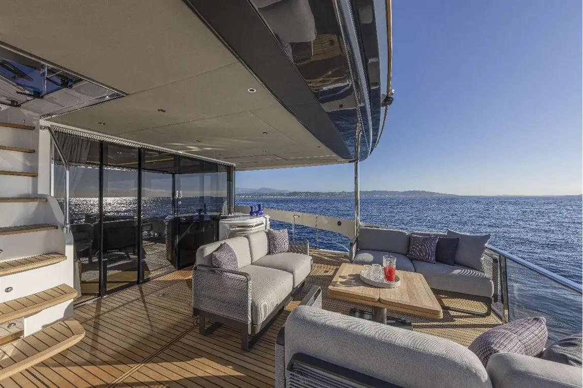 Luxury yacht deck featuring stylish seating, a table with drinks, panoramic sea views, and modern design elements.
